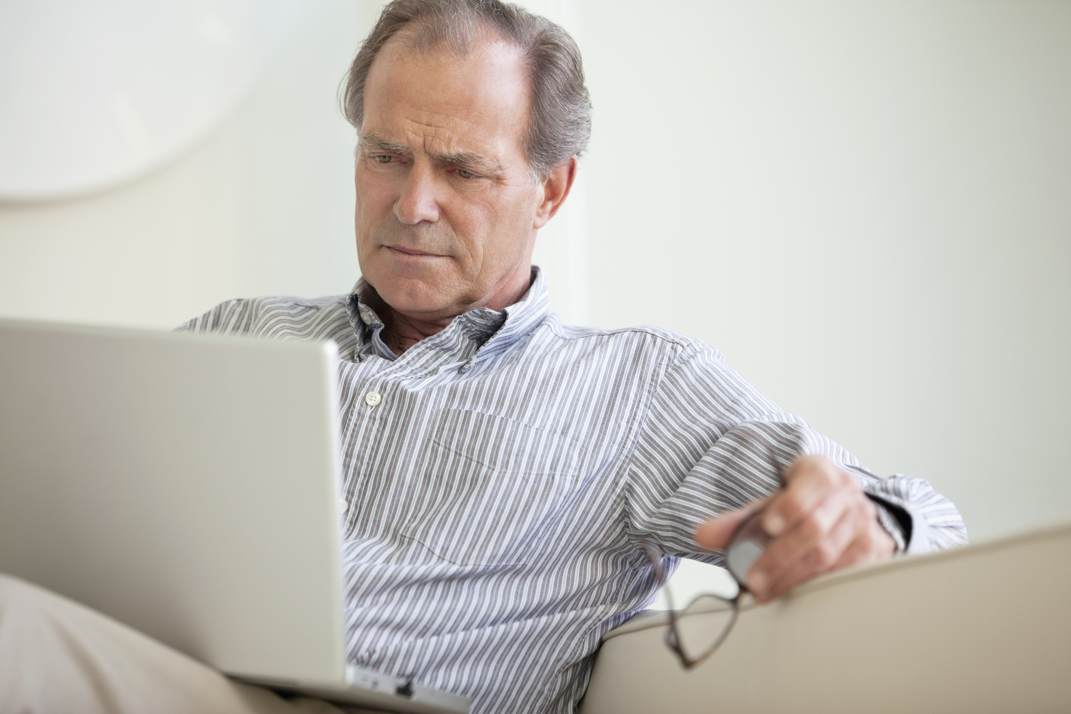 A senior man reading material on his laptop.