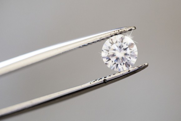 A round diamond being held by tweezers.