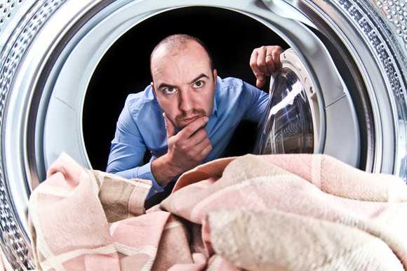 Man staring into a washing machine and pondering, seen from inside the machine's drum