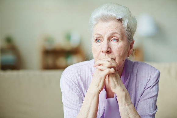 An older woman with her hands clasped in front of her face looking worried.