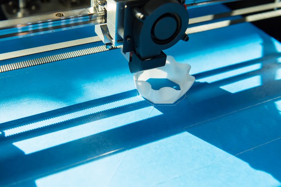 An industrial 3D printer printing a unidentifiable white plastic object.