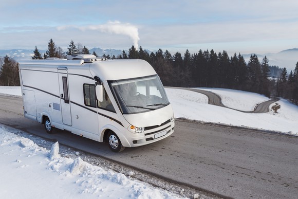 A motor home driving past a snow-covered field.