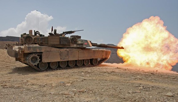 An Abrams tank firing a round atop a hill.