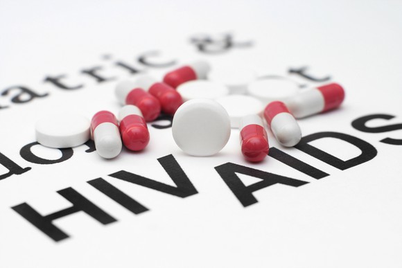 Red-and-white pills on top of white sheet with HIV and AIDS printed on it