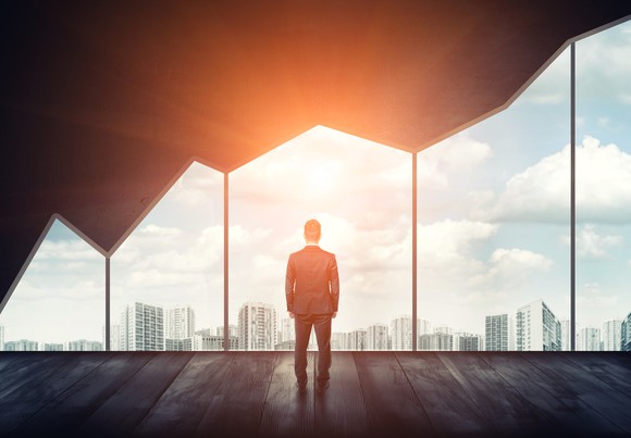 Business man looking out window at a sunset and cityscape with his back to the camera.