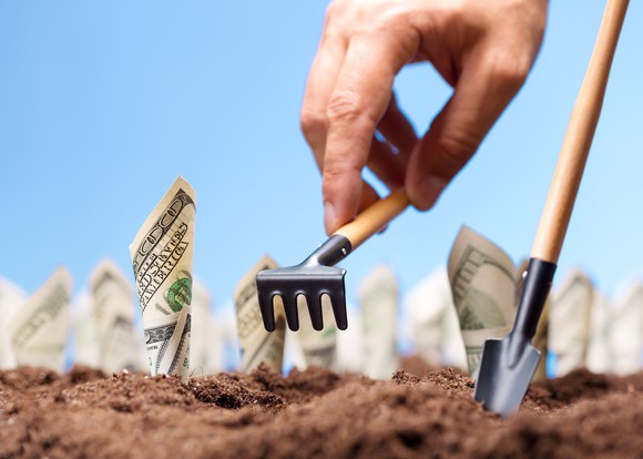 A farmer planting hundred dollar bills in the soil to grow.