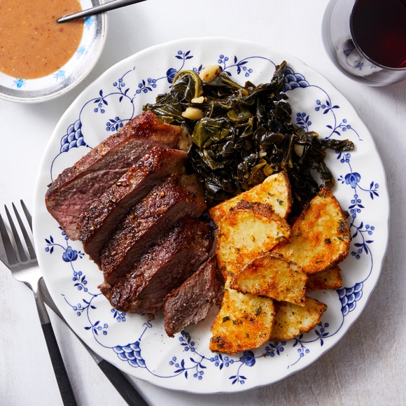 A Blue Apron meal on a white and blue dish featuring beef, potatoes, and kale.