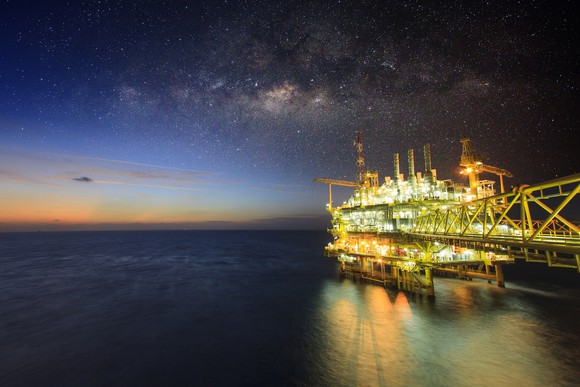An offshore oil platform with its lights on beneath a half-lit sky
