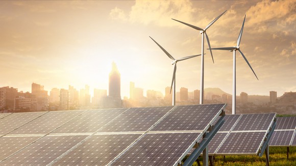 Solar farm with wind turbines and an urban skyline in the background.