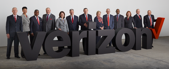 13 people standing behind a 3D representation of the Verizon logo.