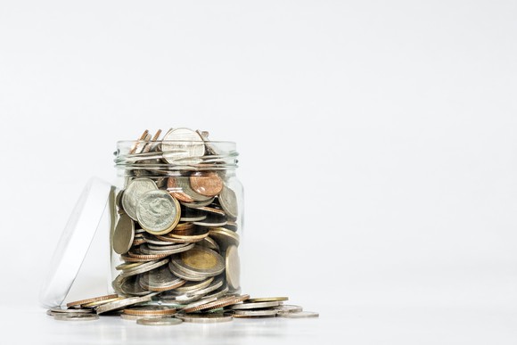 Glass jar loaded with coins, some of which have spilled over