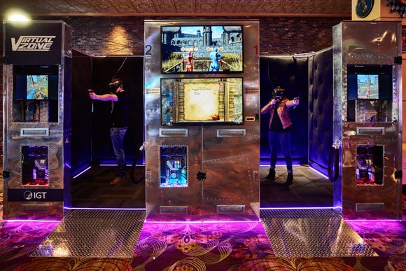 Two people gaming in side-by-side Virtual Zone booths from IGT in a casino.