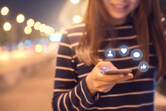 Woman holding phone with icons hovering above it.
