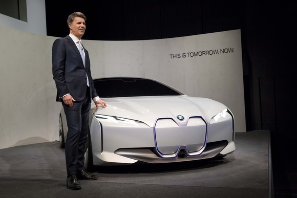 CEO Harald Krueger standing next to a low-slung white sedan, the BMW Vision Dynamics show car.