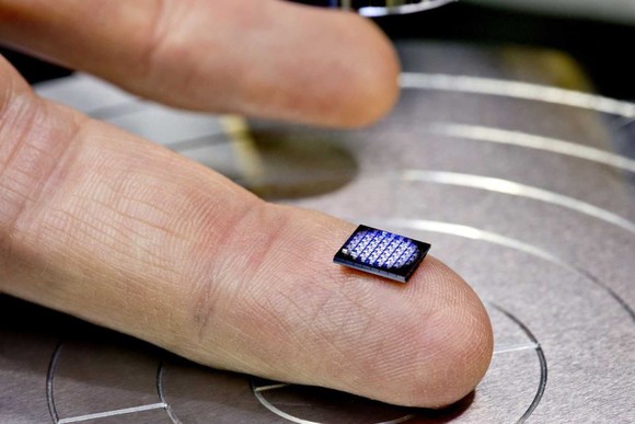 a tiny rectangular computer sits on a person's middle finger.