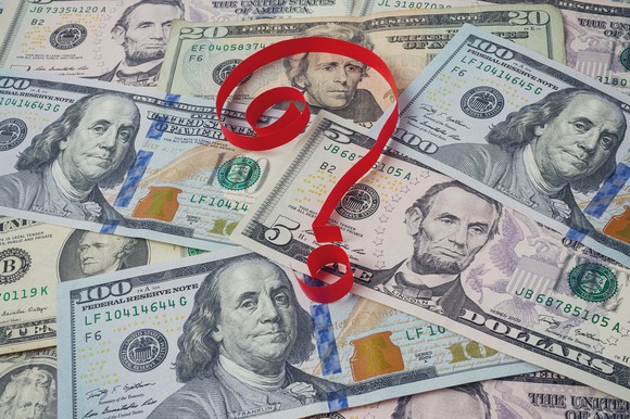 Red ribbon forming question mark on top of cash spread out on surface