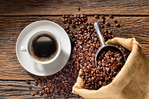 A coffee cup sits in a pool of coffee beans.