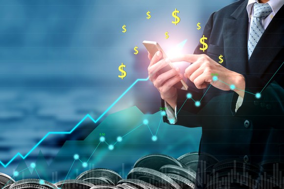 Man holding calculator with dollar signs shown around it and line charts going up in foreground