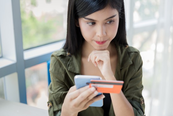 young woman resting chin on fist and holding smartphone and credit card