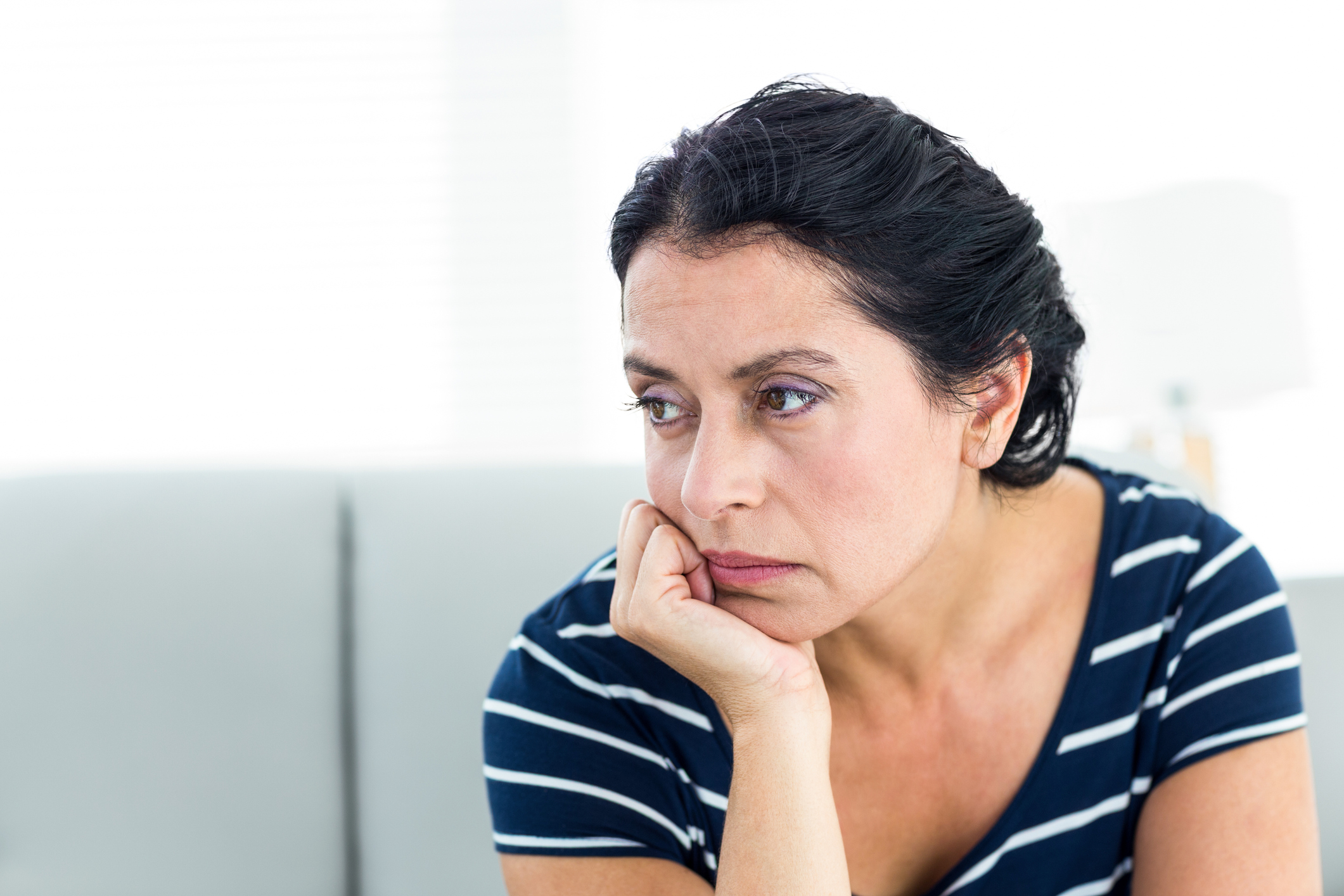 A woman, seated, looks away unhappily with her chin resting on her hand.