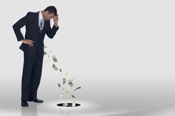 Person watching money getting sucked out of his pocket into a hole in the floor.