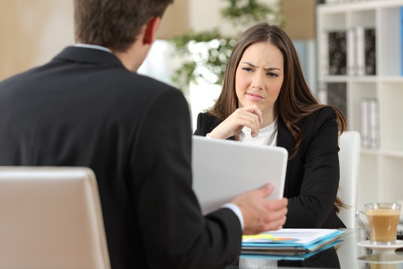 A woman looks skeptically across the table at a tablet a man is showing her.