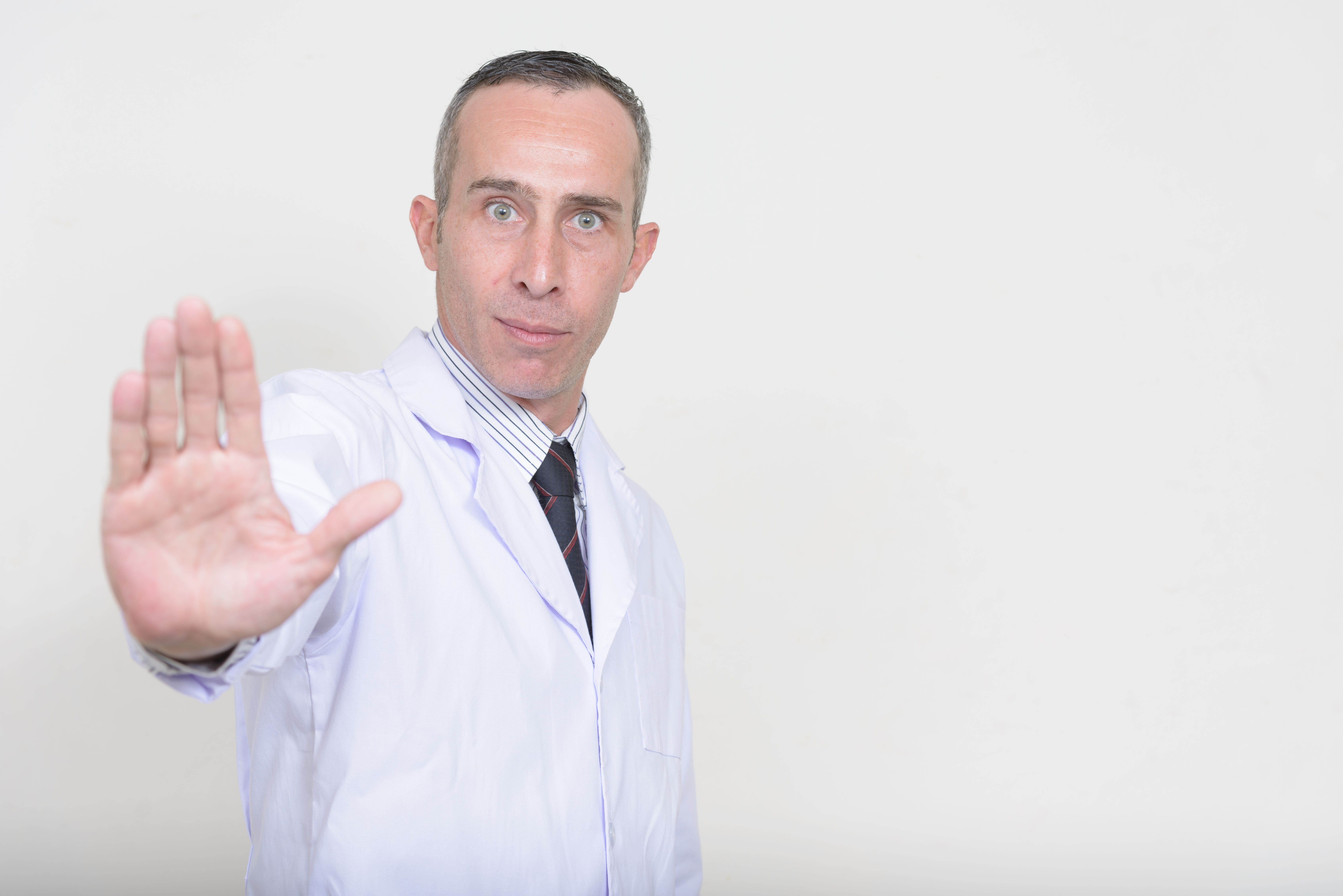 A man in a lab coat holds his hand up with the palm facing out