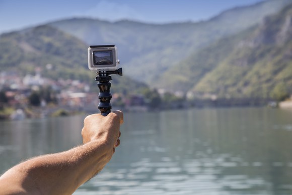 A person holding a GoPro camera in their outstretched hand on the water.