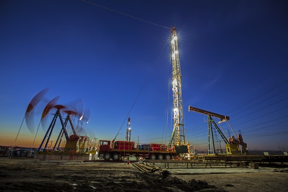 Oil pumps working the the background near a drilling rig at dusk.