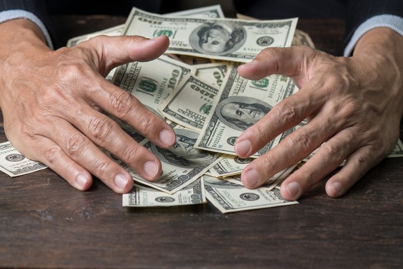 Businessman pulling pile of $100 bills off a table.