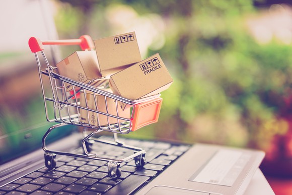 A miniature shopping cart with boxes in it on top of a laptop keyboard.