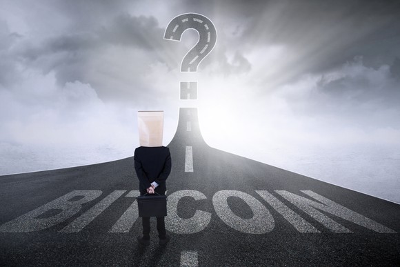 A man standing on a road labeled "Bitcoin" that ends in a question mark