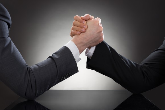 Two people in suits arm wrestling.
