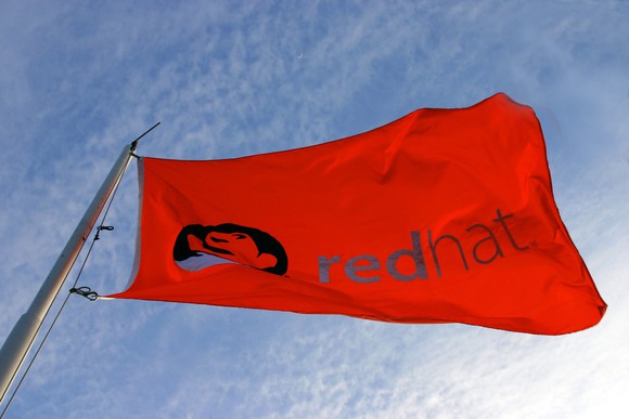A red flag emblazoned with Red Hat's logo, fluttering in the wind.
