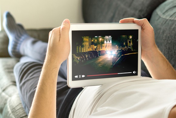 A person lying on a couch holds a tablet playing a video.