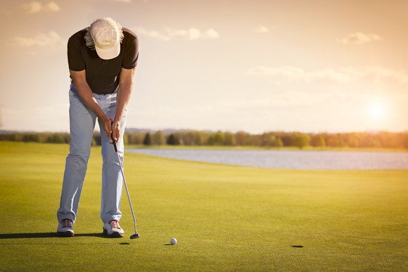 Man looking down at his golf club while playing on a golf course
