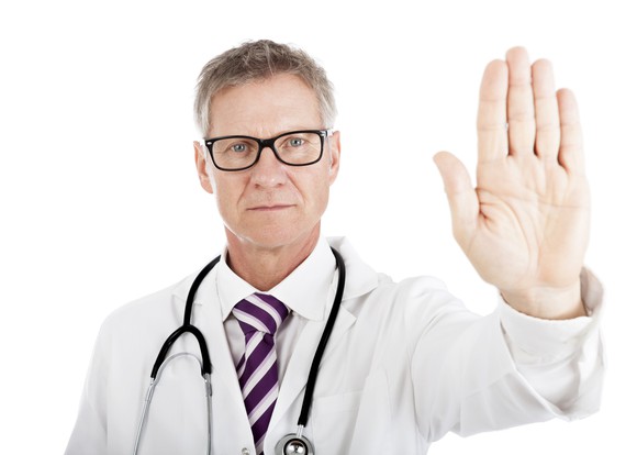 Man in lab coat holding up hand with palm facing outward