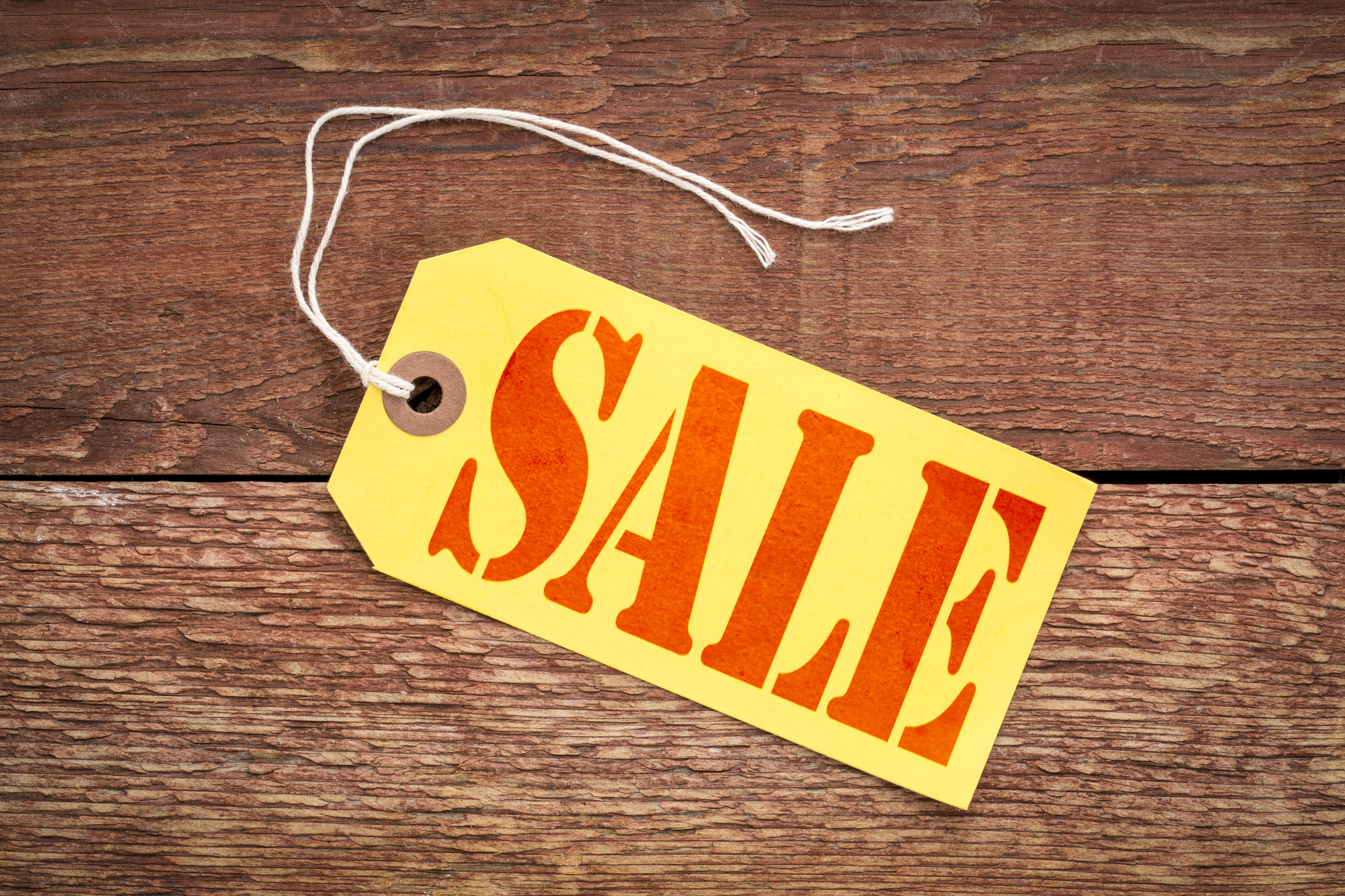 A sale sign on a yellow paper price tag against rustic wood.