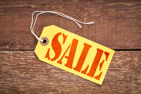 A sale sign on a yellow paper price tag against rustic wood.
