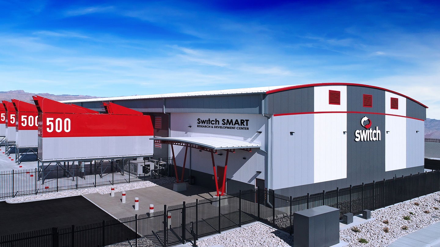 Warehouse structure with Switch logo on side and various modular data center products attached to the side.