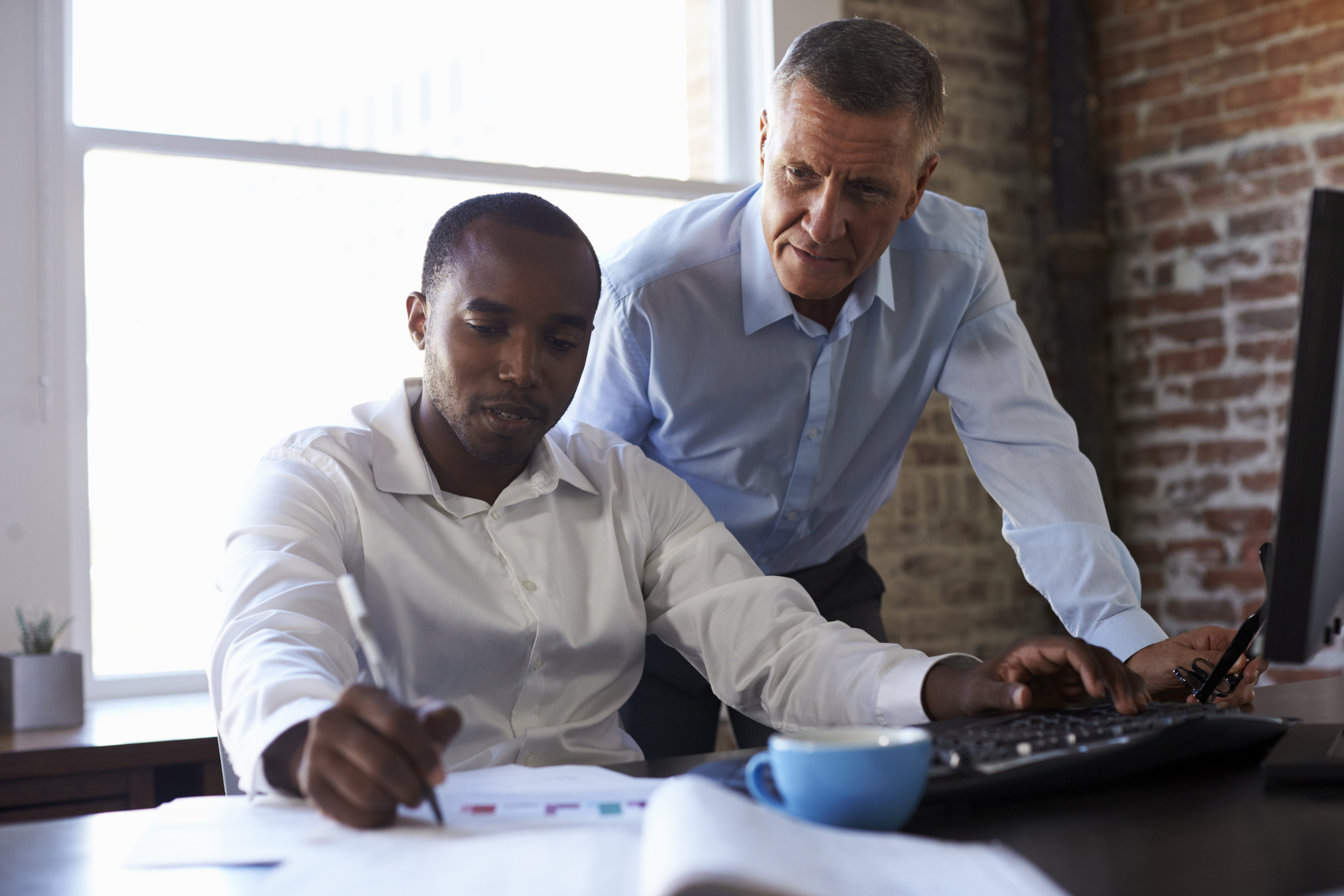 Man working at a desk while another man looks over his shoulder