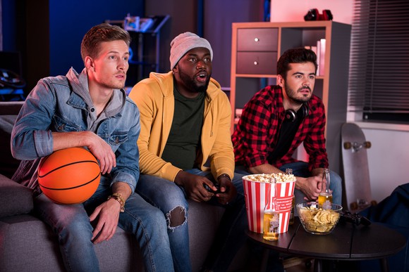 Three male fans sitting on a couch watching a game.