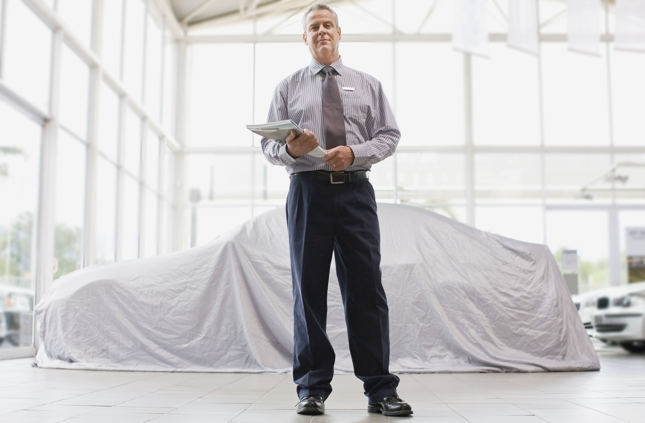 A salesman stands in front of a showroom car that's covered with a white dropcloth.