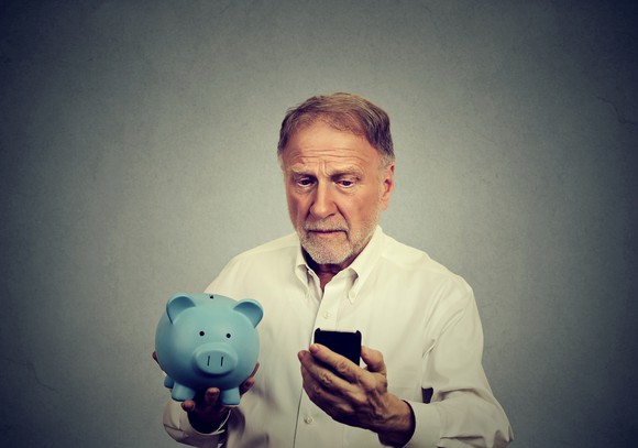 Older man holding a blue piggy bank and looking at a phone