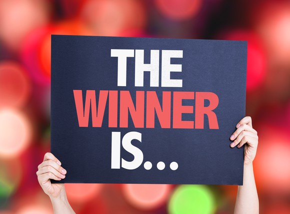 hands holding a sign saying The Winner Is...