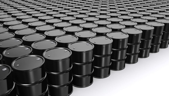 A large number of oil barrels placed in organized rows and columns in a white room.