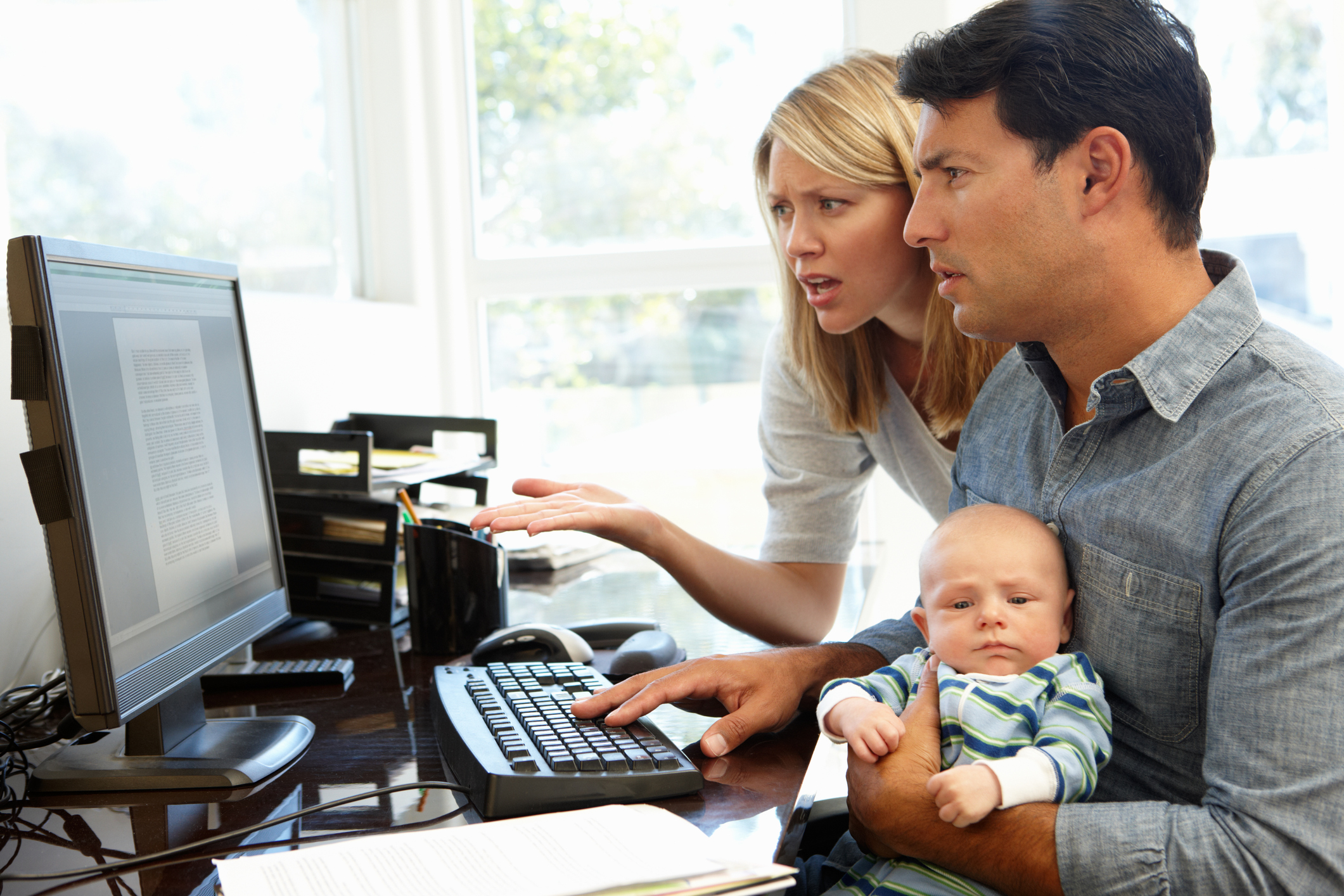 Worried parents holding a baby and reading an online article.