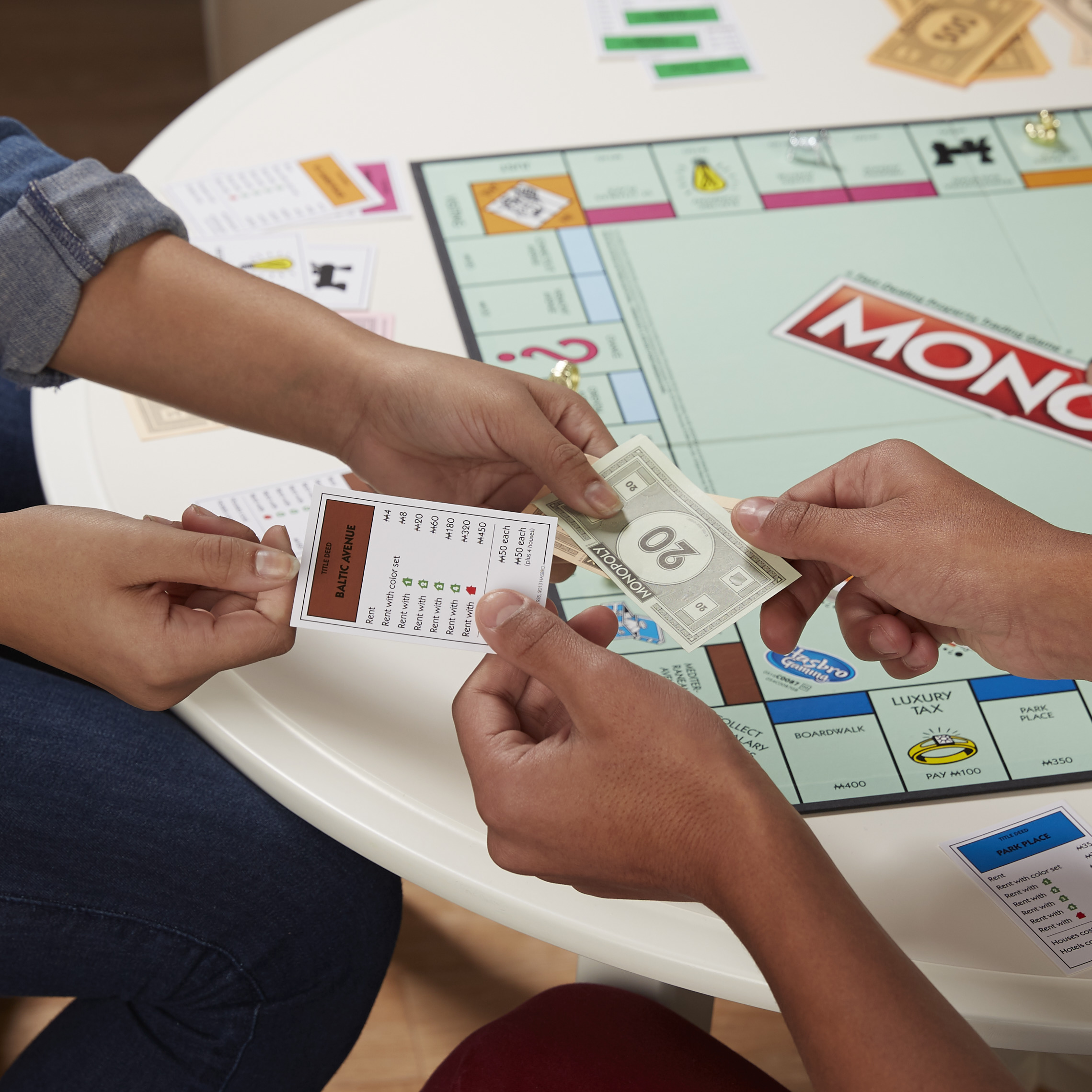 People playing Monopoly game, with one handing over game cash, while the other hands over property card.