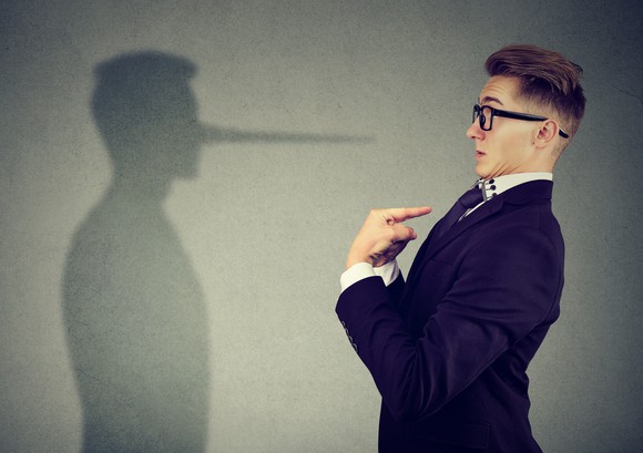 A man in a suit looks at a shadow with a long nose.