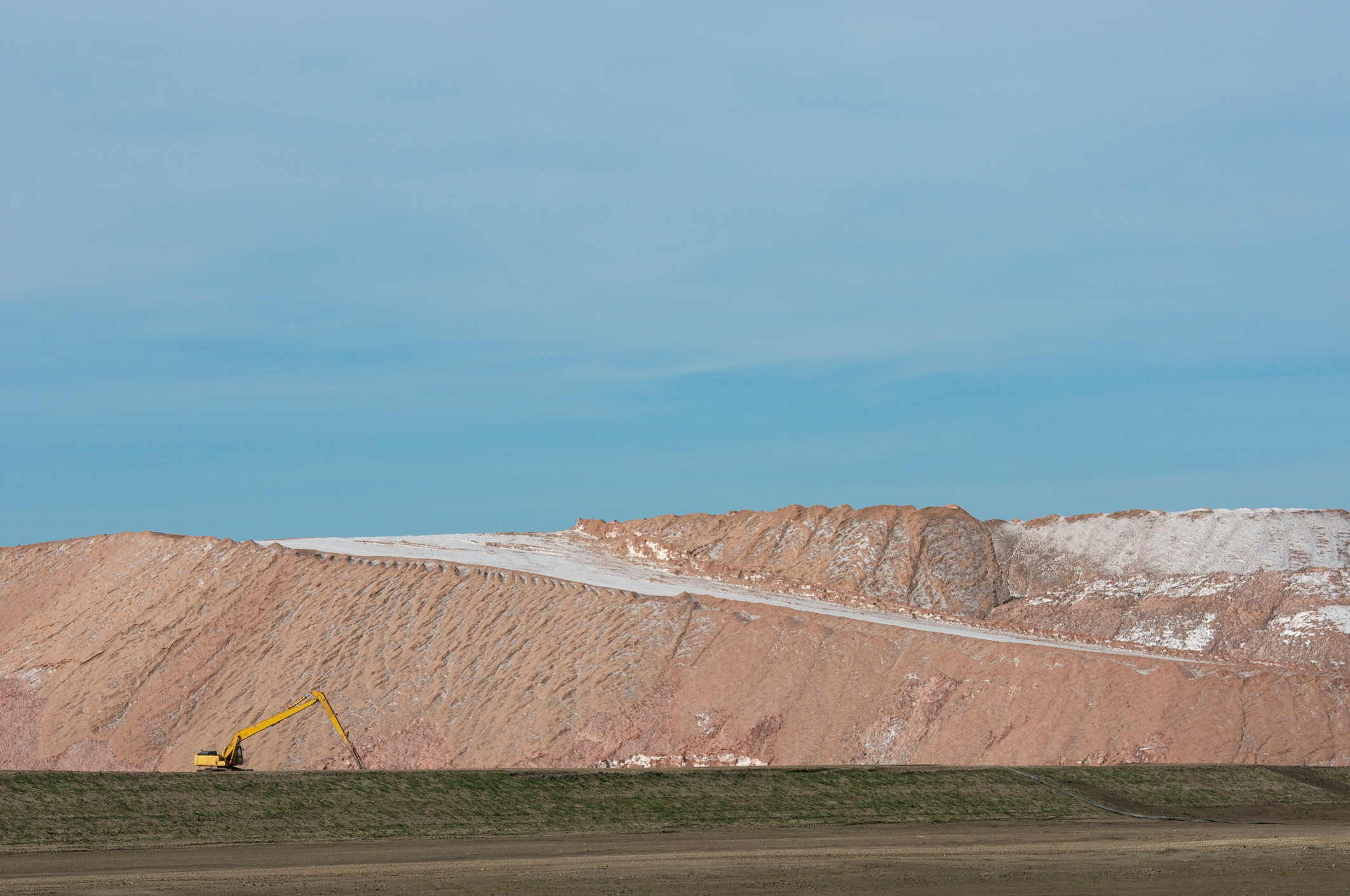 Hill of mined potash with a backhoe in front of it